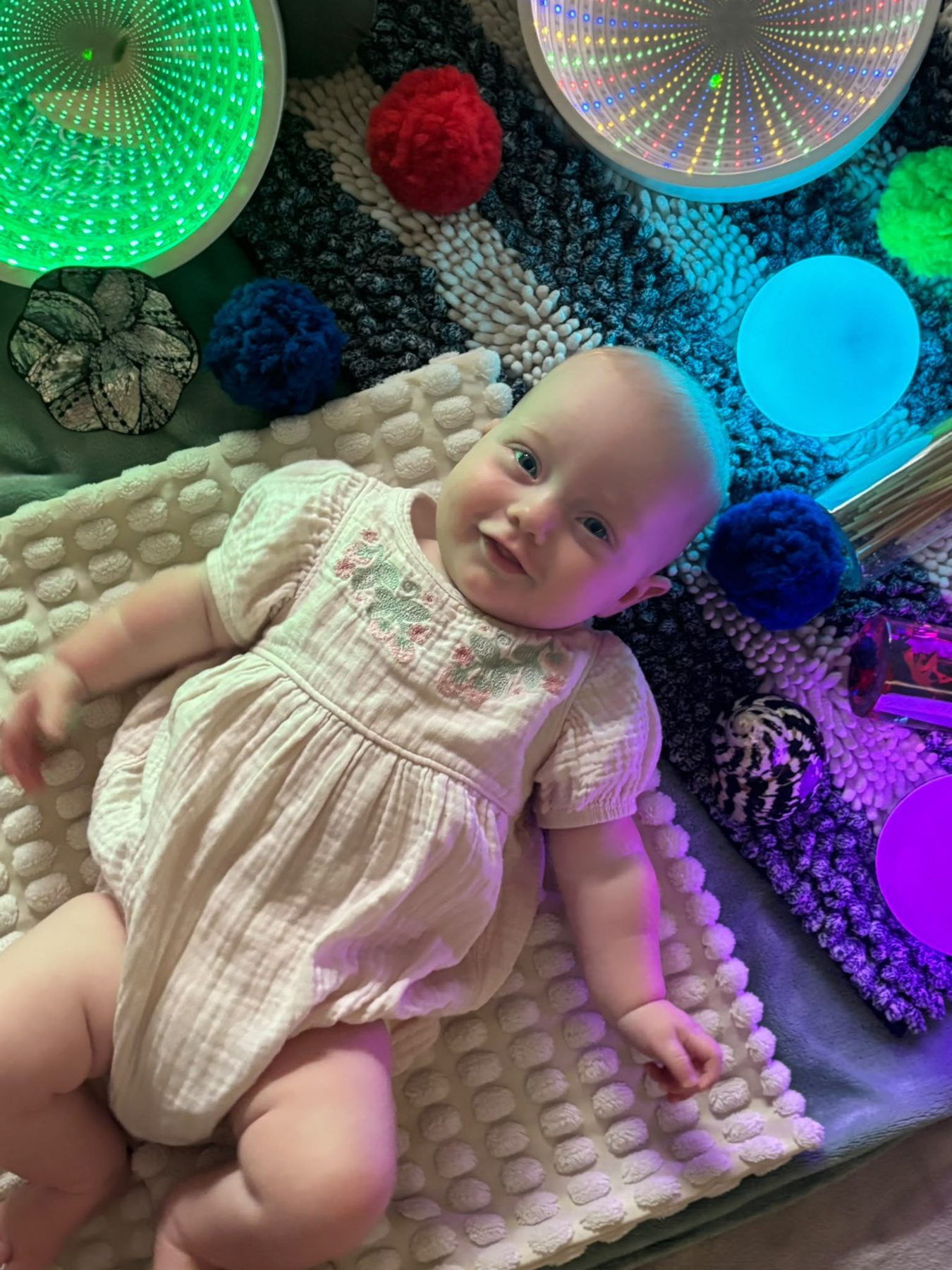 A smiling baby lying among glowing sensory lights and textured blankets