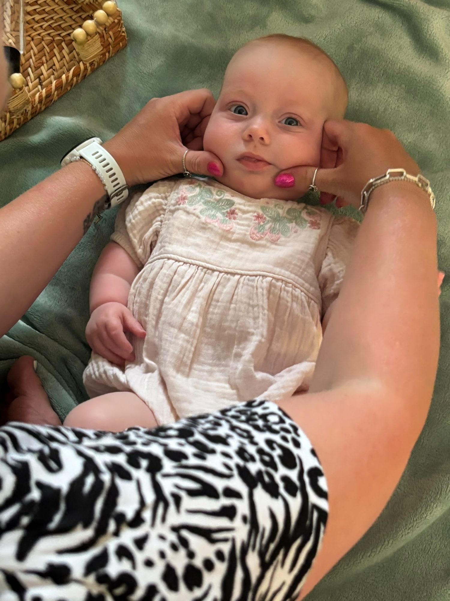 A baby resting contentedly in Jess arms on a sage green blanket at a Cosy Cocoon class in Medway