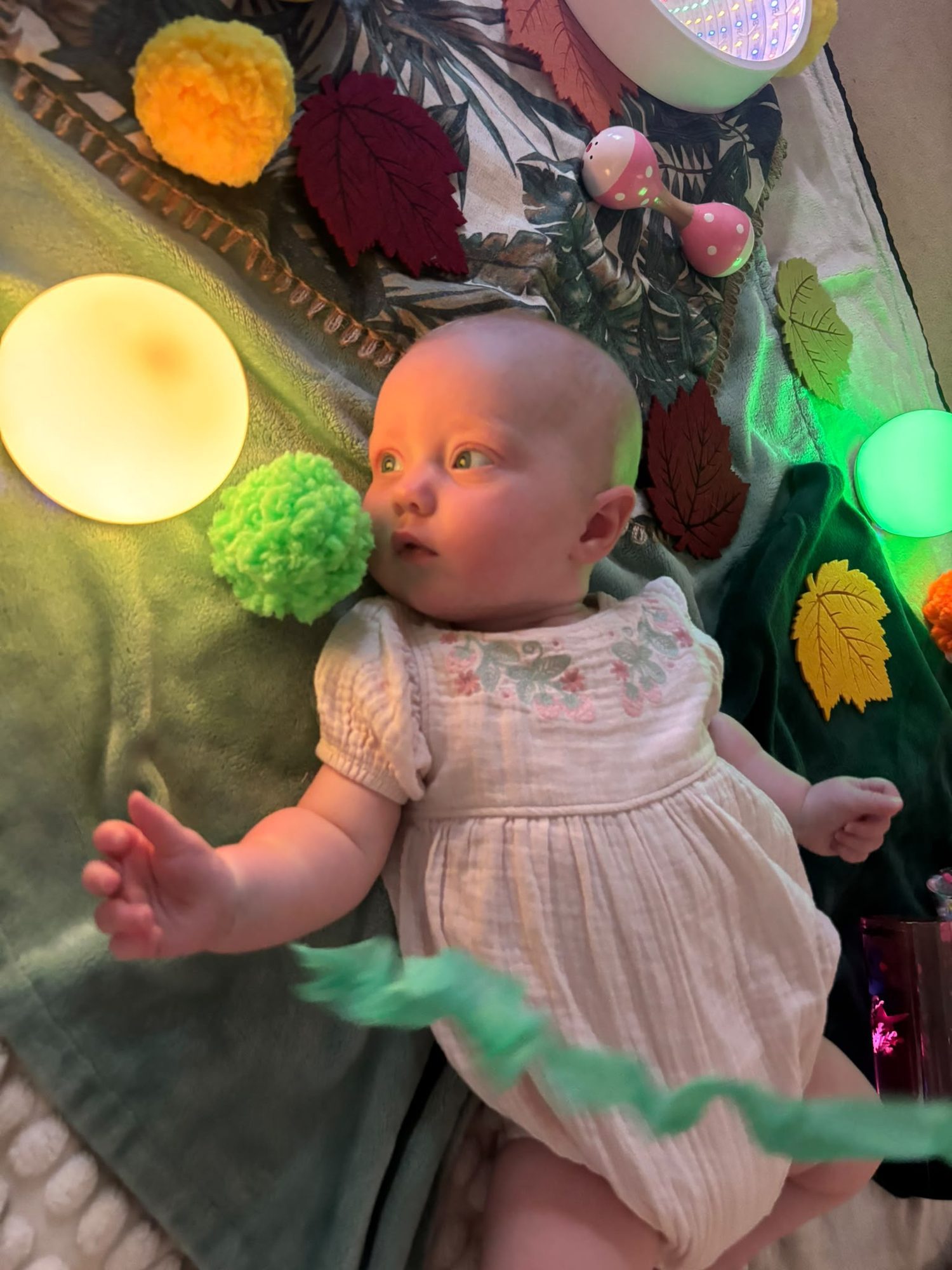A baby lying among soft sensory toys and coloured lights during a Little Wanderers class