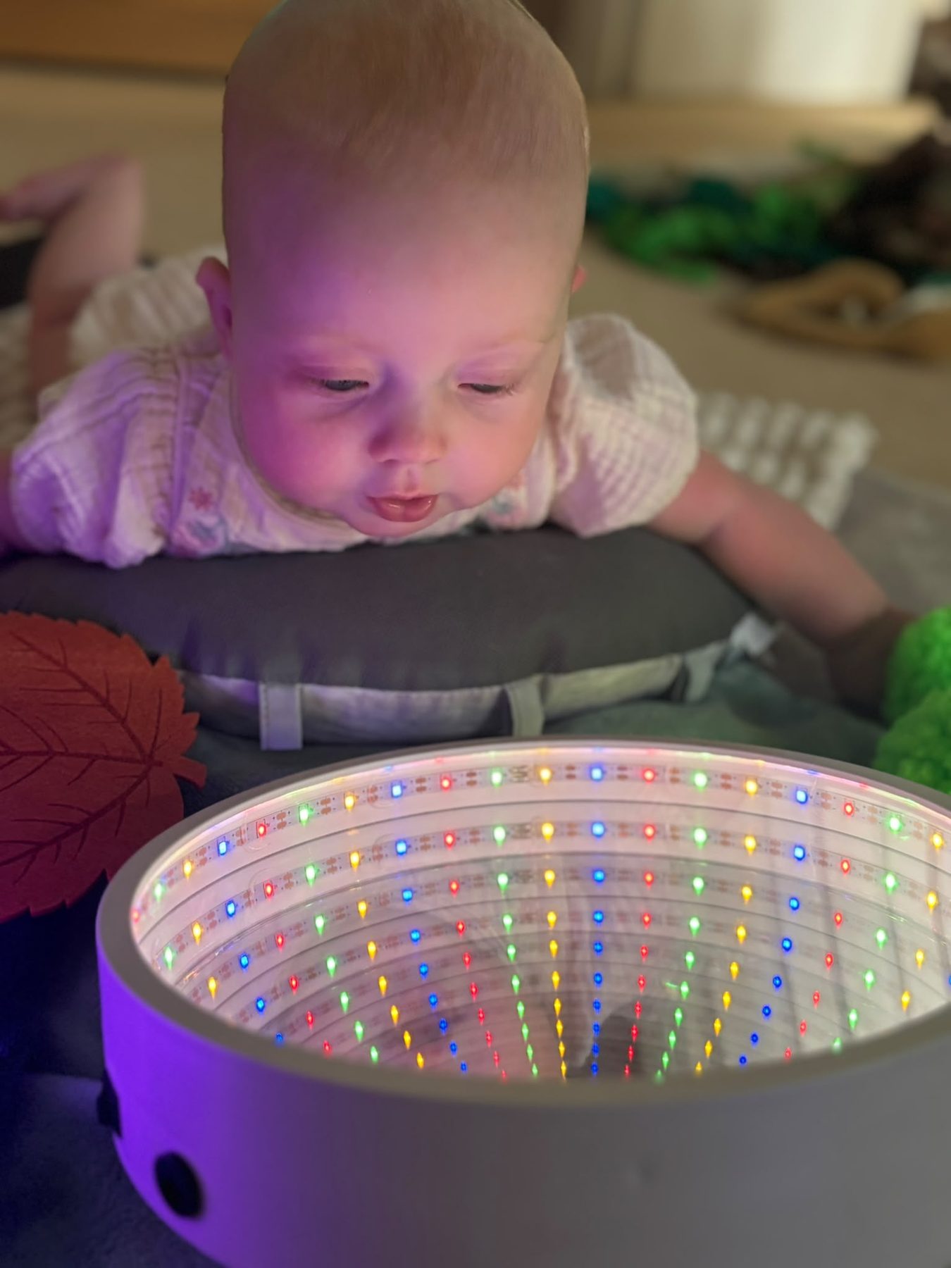A baby doing tummy time propped on a cushion, watching a colourful sensory light